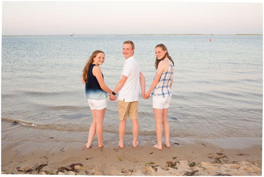 Three siblings hold hands at the beach