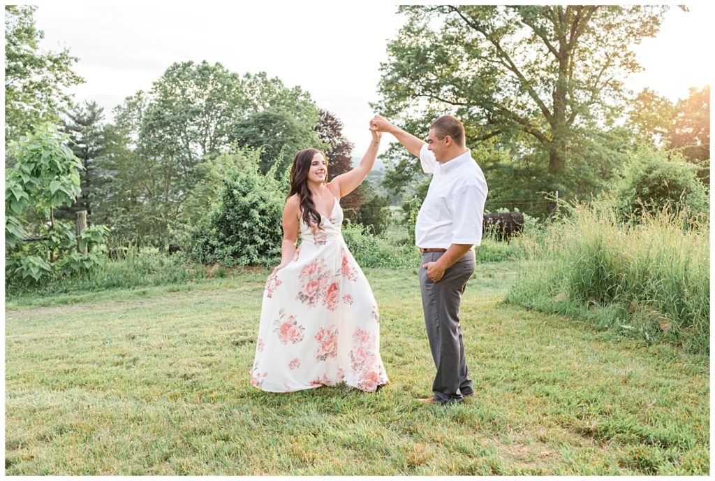 A man twirls his fiance on top of a hill