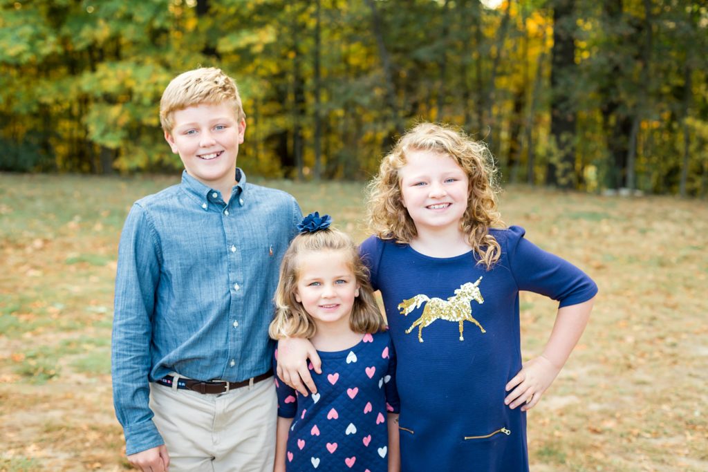 Three siblings dressed in blue stand together and smile