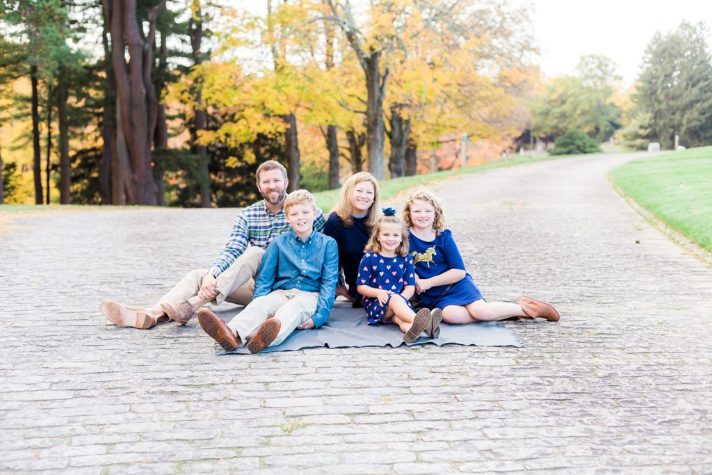 A family sits on a blanket on a brick road.