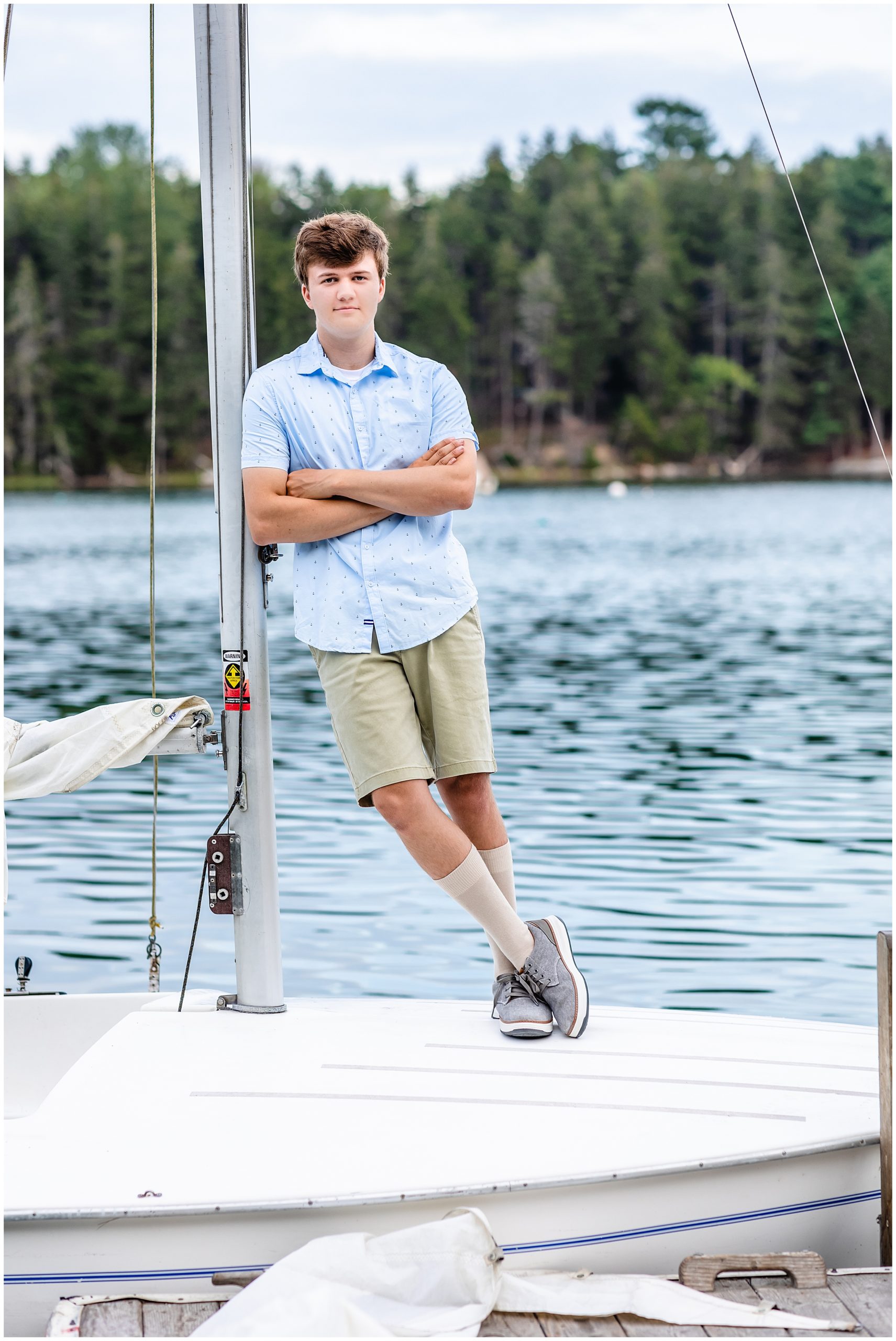 Boy in tan shorts leans against mast of sailboat