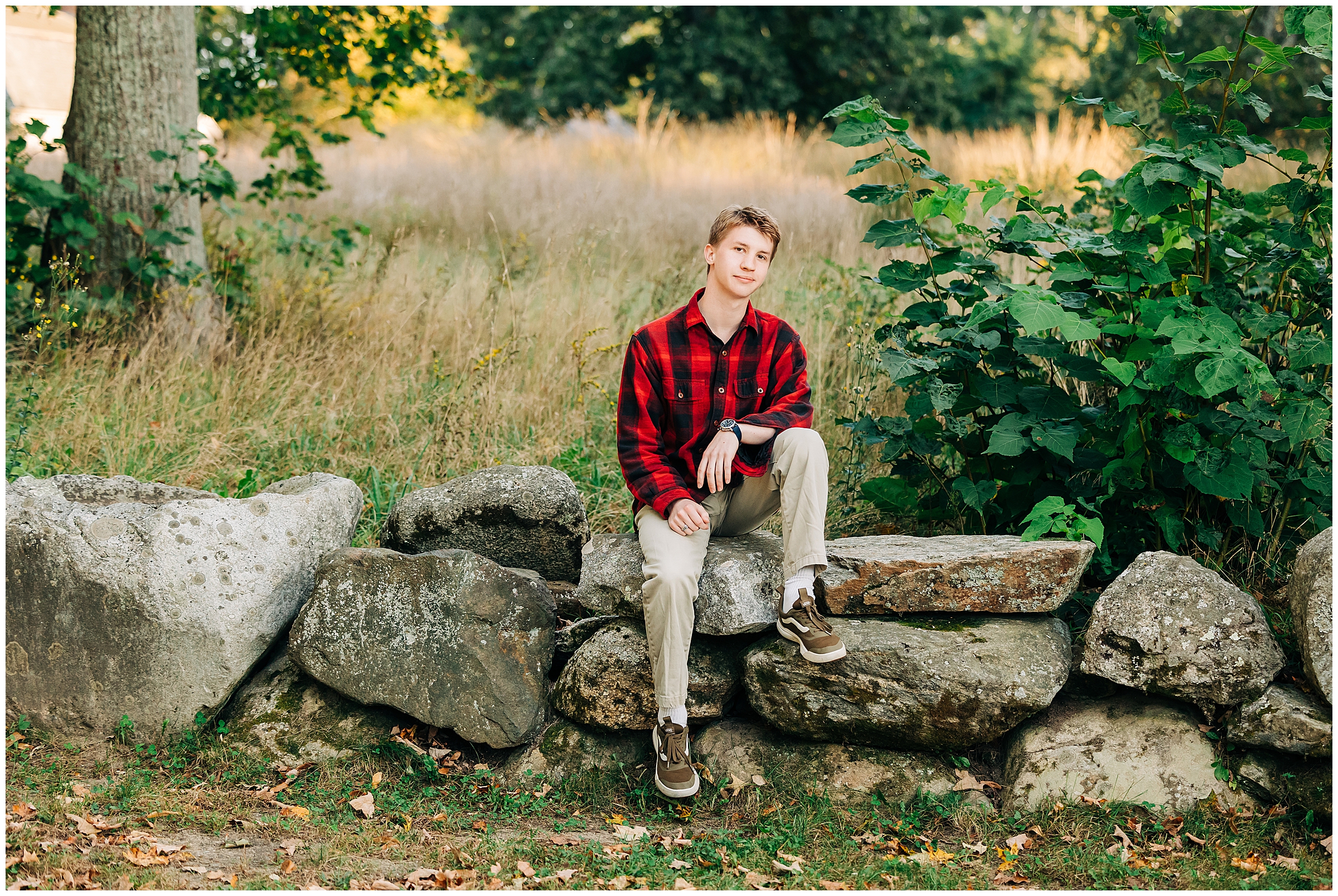 A boy in a plaid shirt sits on a rock wall